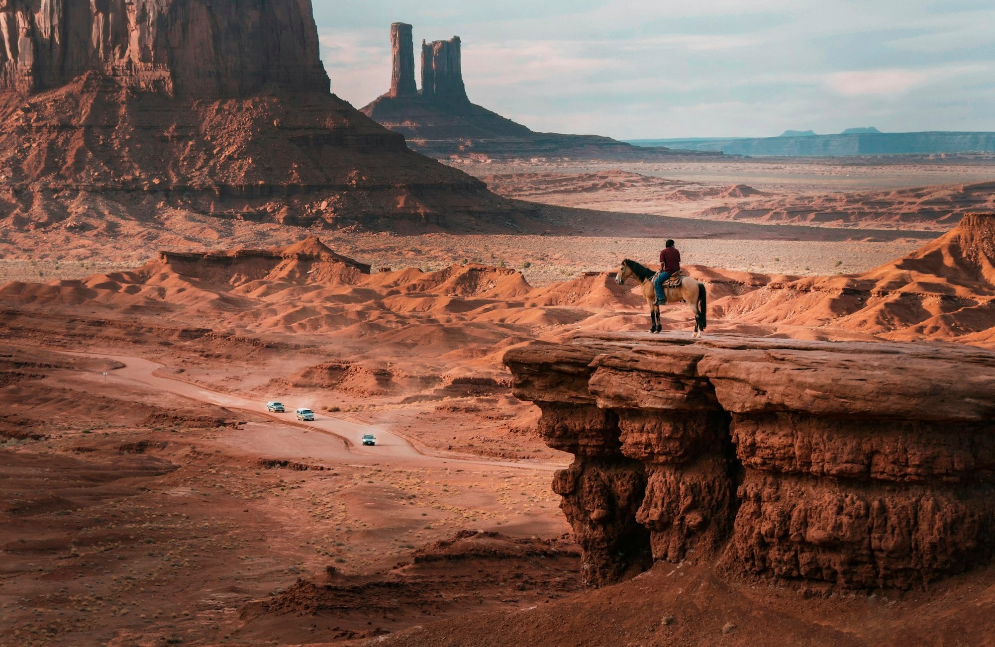 A rider on a sandstone ledge above Monument Valley in bright sun